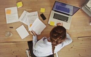 High angle view of an young brunette working at her office desk with documents and laptop. Businesswoman working on paperwork.